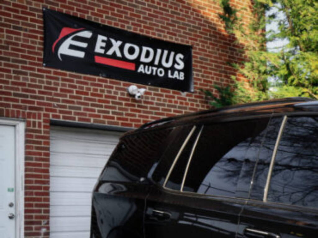 Black SUV parked outside Exodius Auto Lab with the shop sign visible on a brick building.
