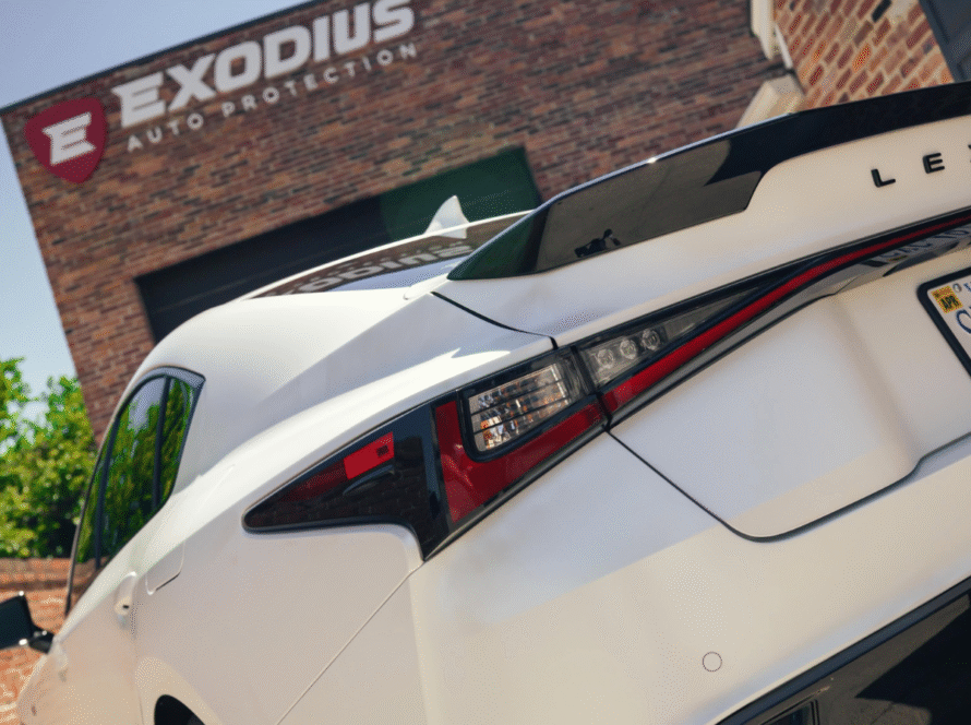 White Lexus rear view with stylized tail lights parked in front of Exodius Auto Protection shop