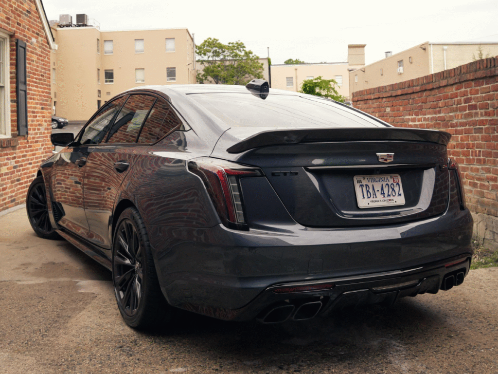 Rear view of dark gray Cadillac CT5 with quad exhaust diffuser and gloss black spoiler parked in alley
