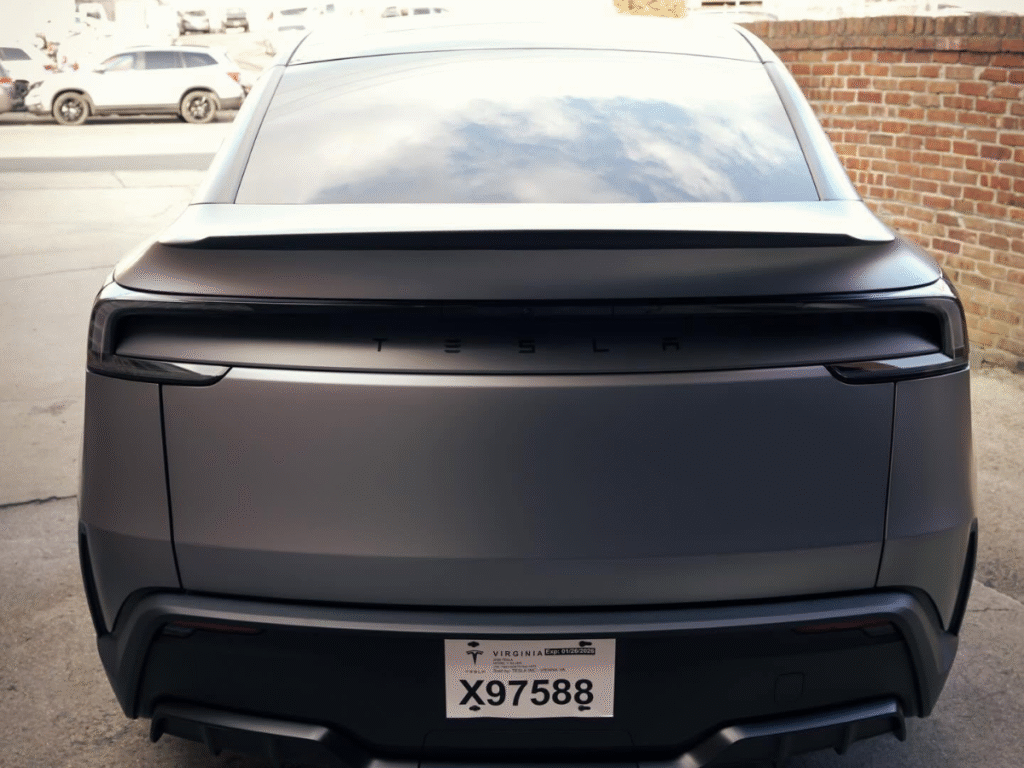 Rear view of matte gray Tesla Model Y with Virginia temporary license plate parked outside brick building