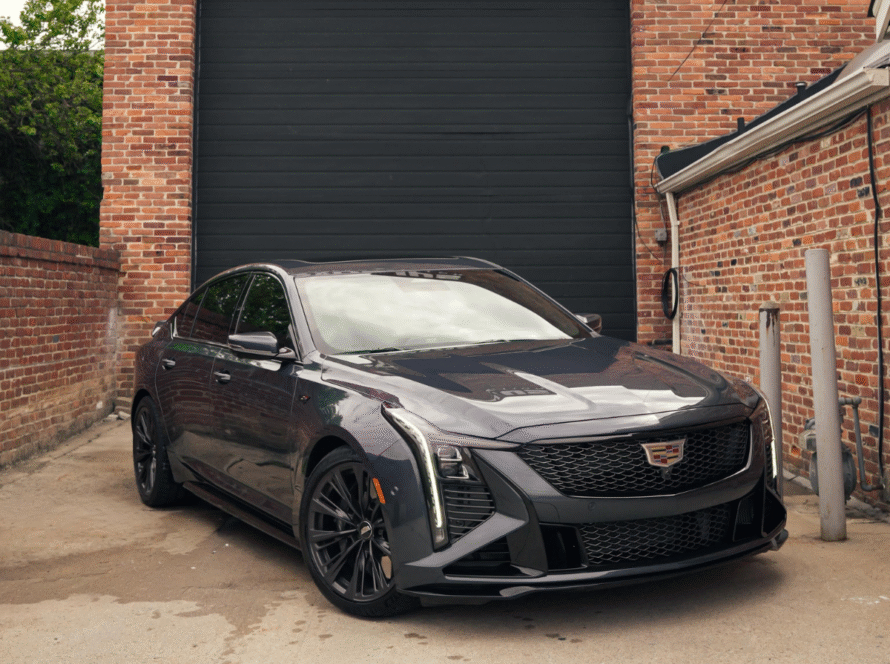 Dark gray Cadillac CT5-V with black alloy wheels and sport grille parked outside brick building auto shop