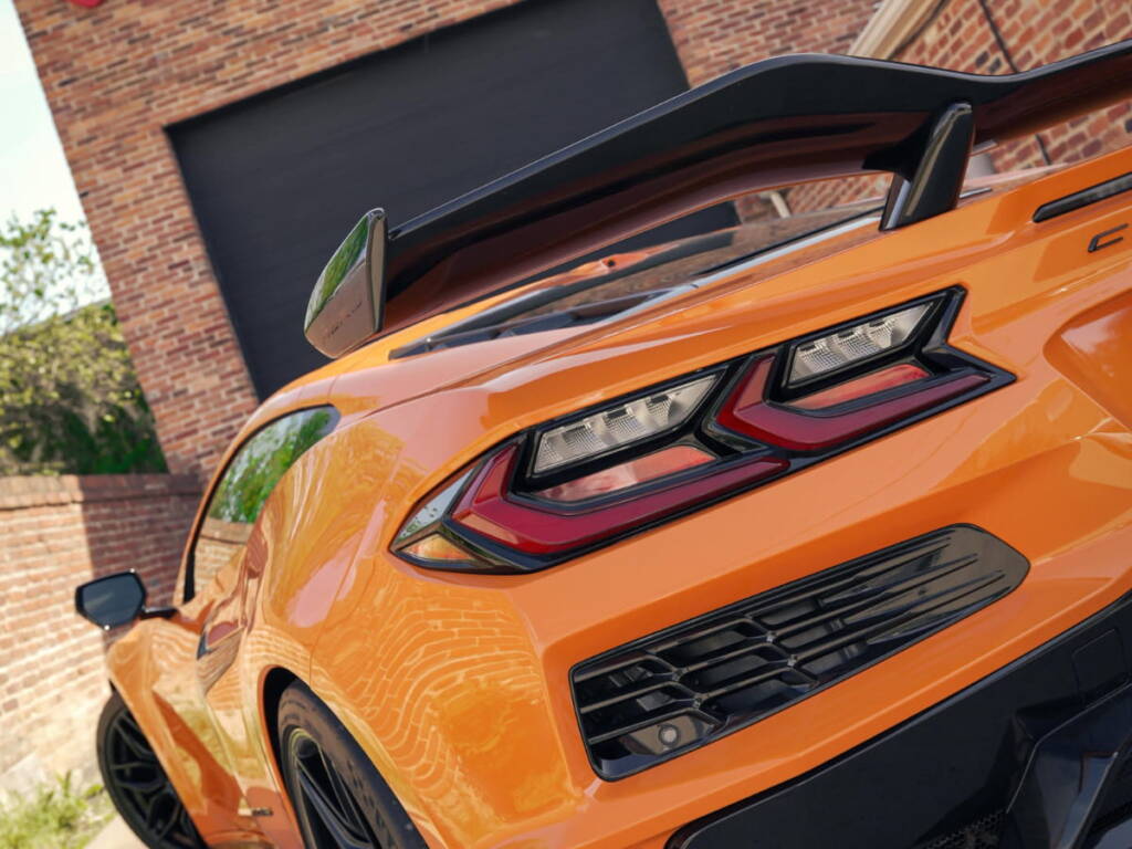 Orange sports car rear detail with spoiler and taillights outside an auto protection shop.