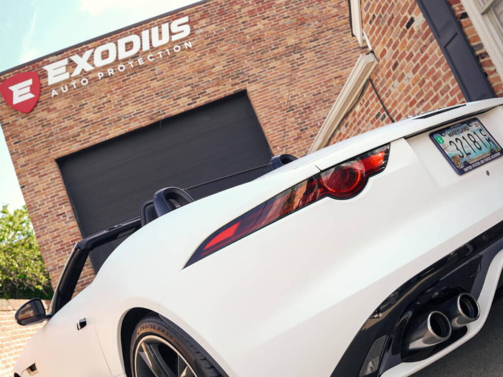 White sports car parked outside Exodius Auto Protection, showing the rear taillight and glossy protected finish.