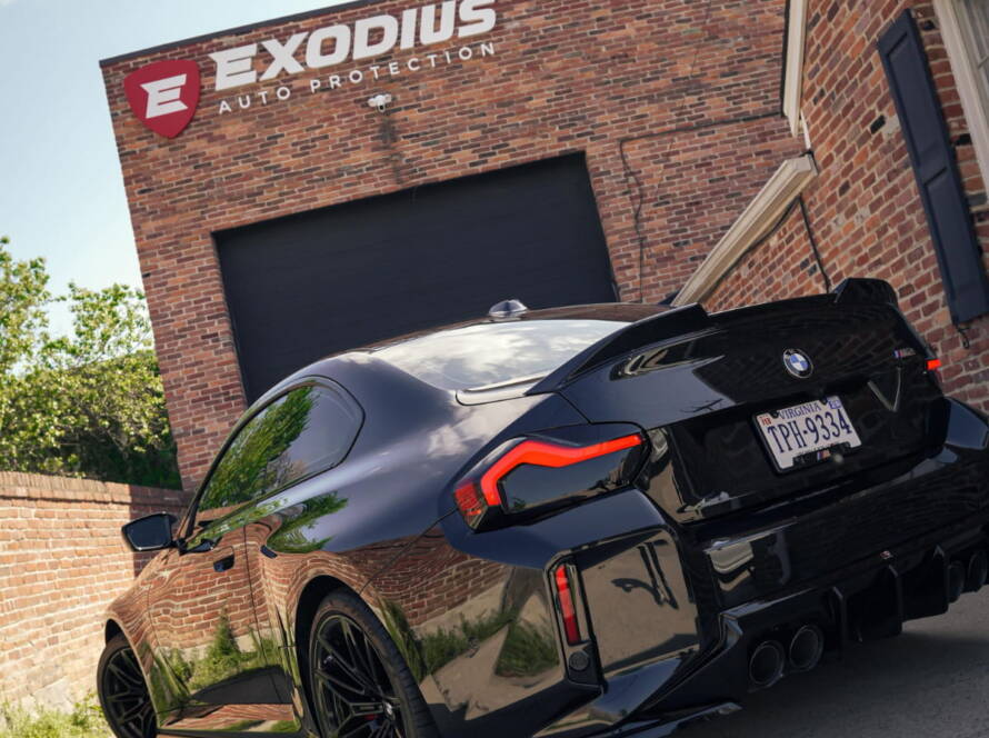 Black BMW M4 parked outside Exodius Auto Protection, viewed from the rear.
