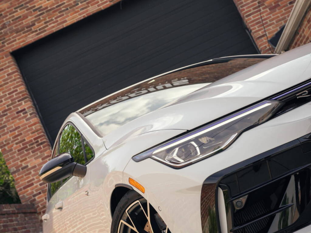 Close-up of the front headlight and bodywork of a white vehicle outside a brick building.