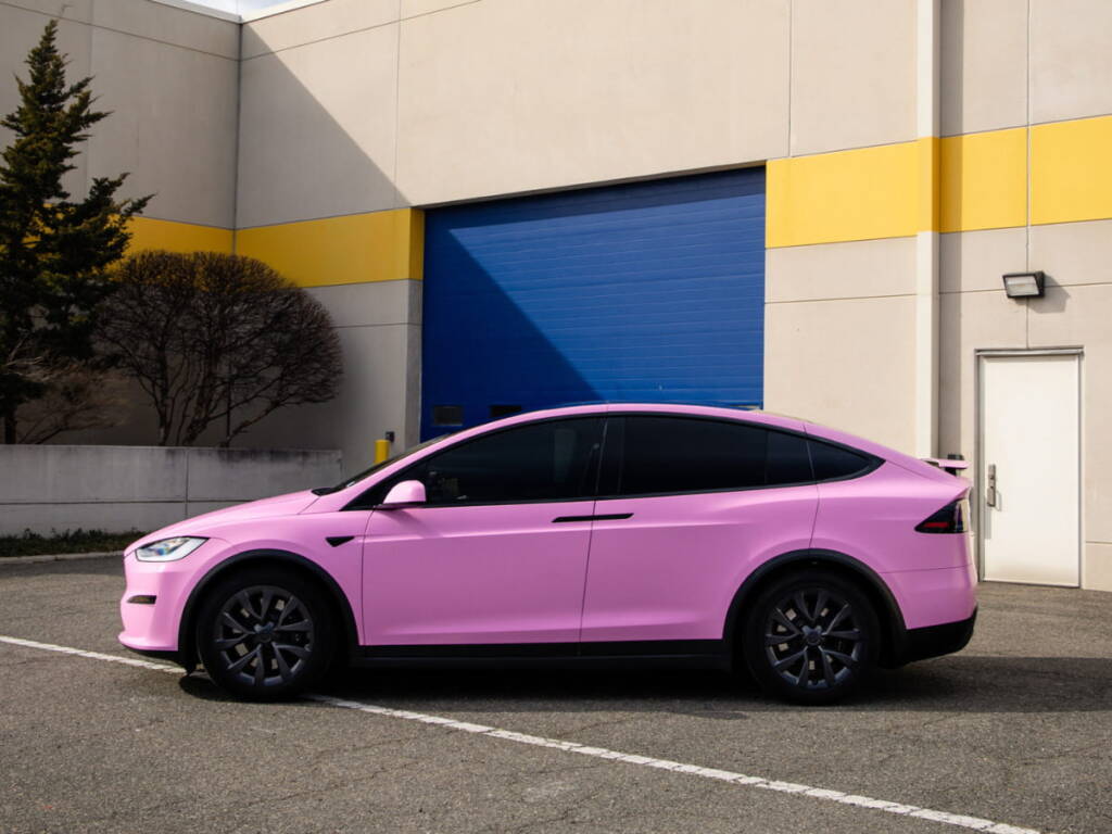 Pink Tesla Model X with dark tinted windows parked outside an industrial building.