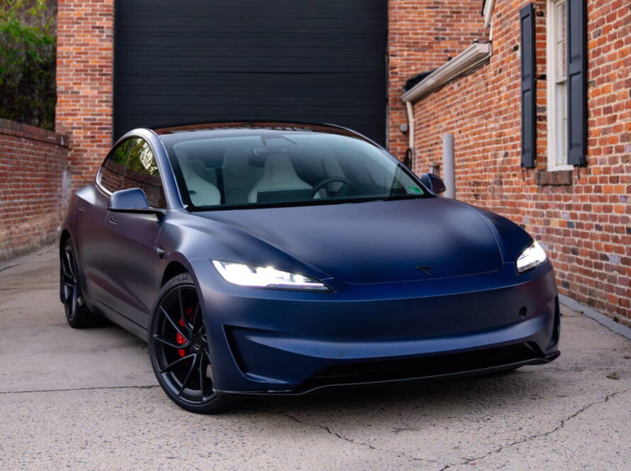 Dark blue Tesla Model 3 parked outside a brick building.