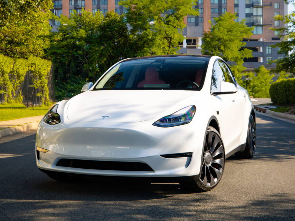 White Tesla Model Y parked on a tree-lined street.